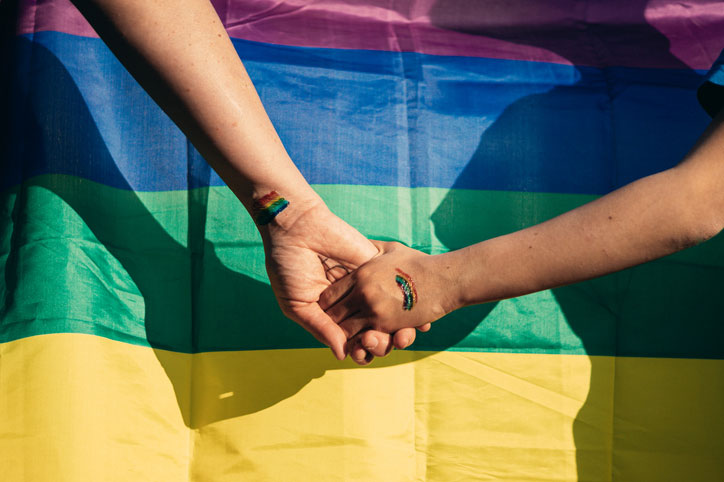 holdig hands in front of rainbow flag